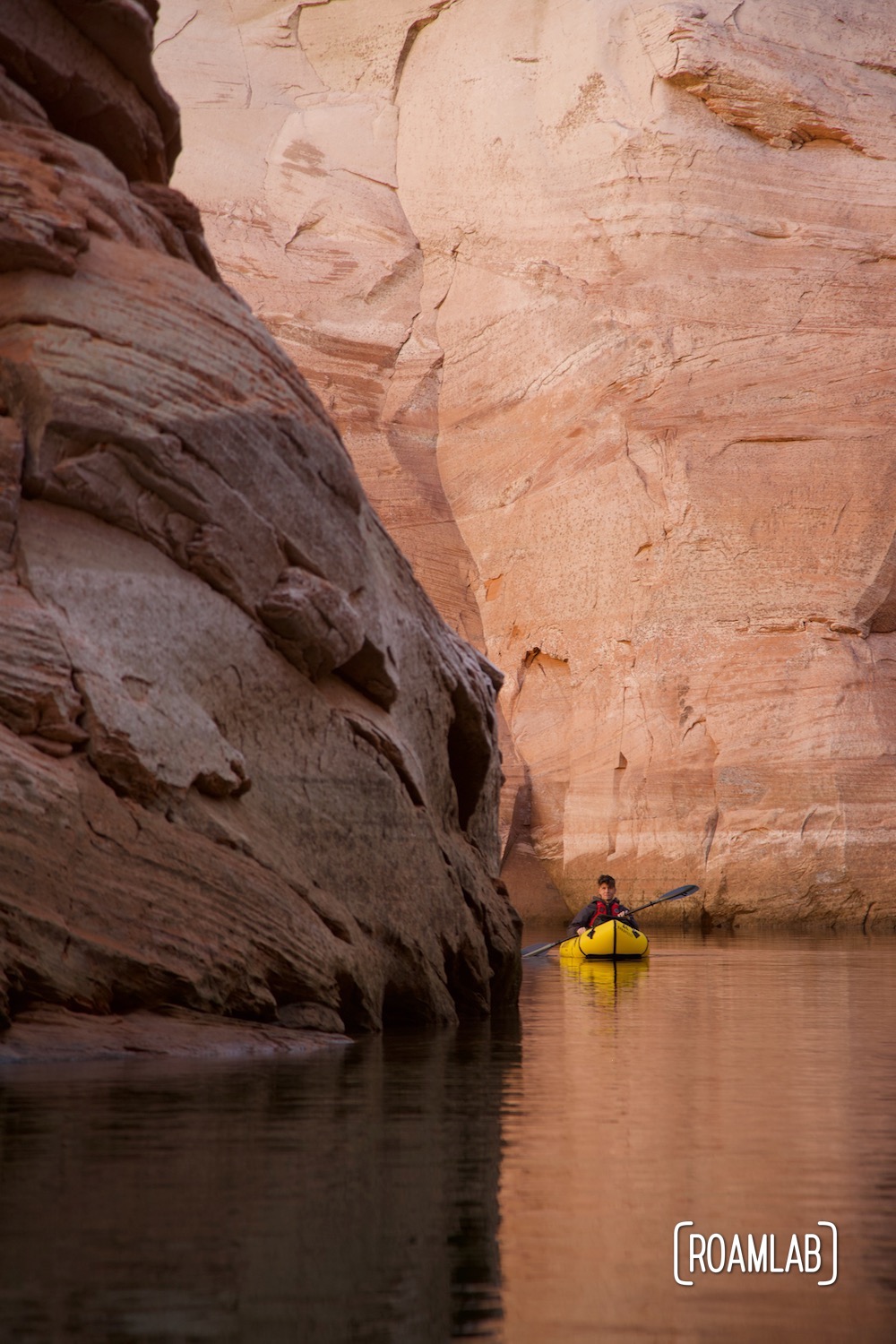 Man in a yellow raft paddling around a corner of pink sandstone cliffs in Antelope Canyon off Lake Powell in Norther Arizona.