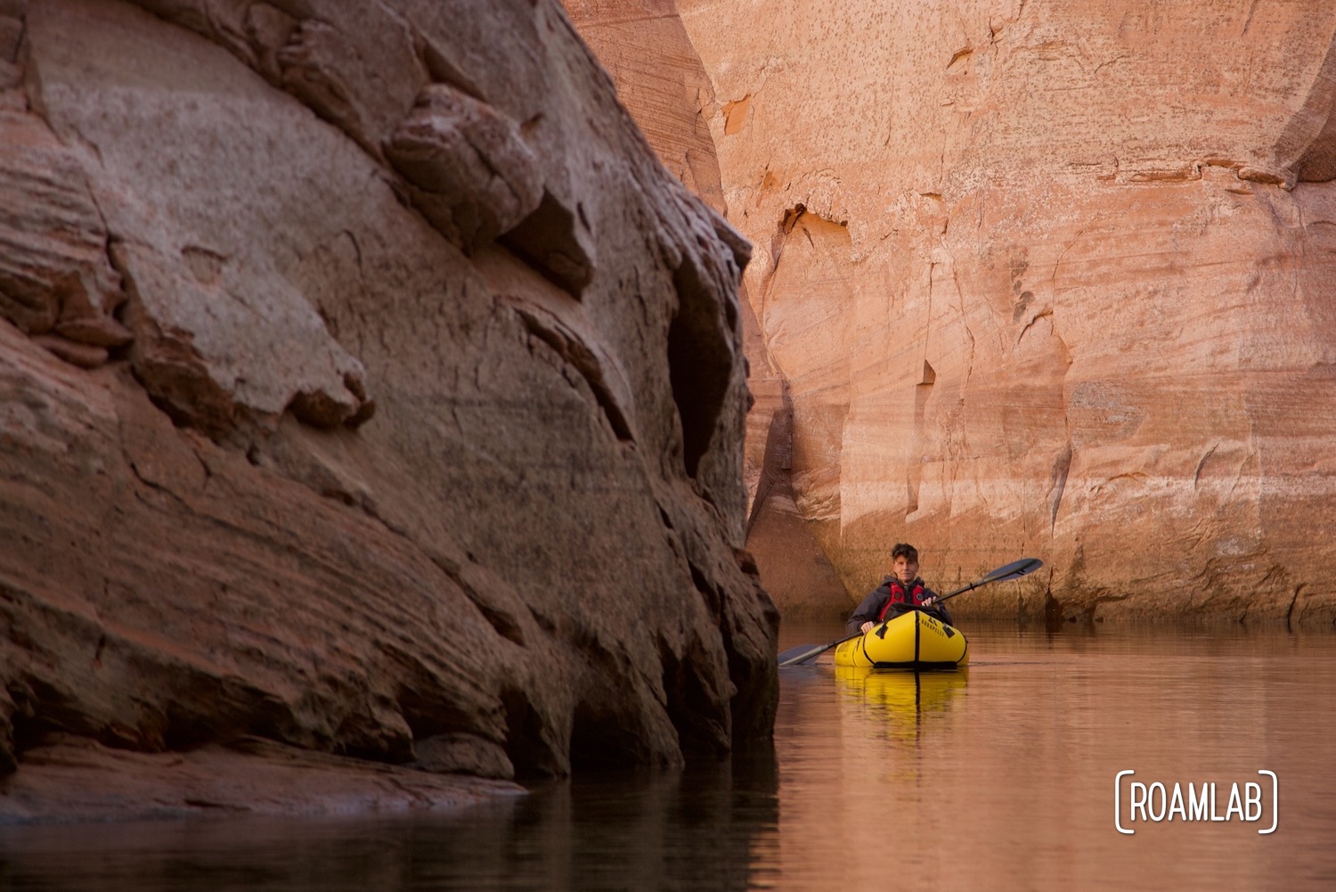 Man in a yellow raft paddling around a corner of pink sandstone cliffs in Antelope Canyon off Lake Powell in Norther Arizona.