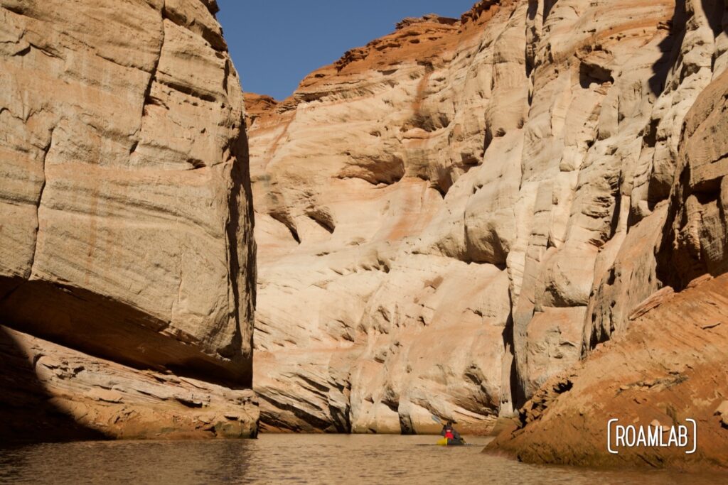 Towering pink cliffs of Antelope Canyon dwarfing a man paddling in a yellow raft.
