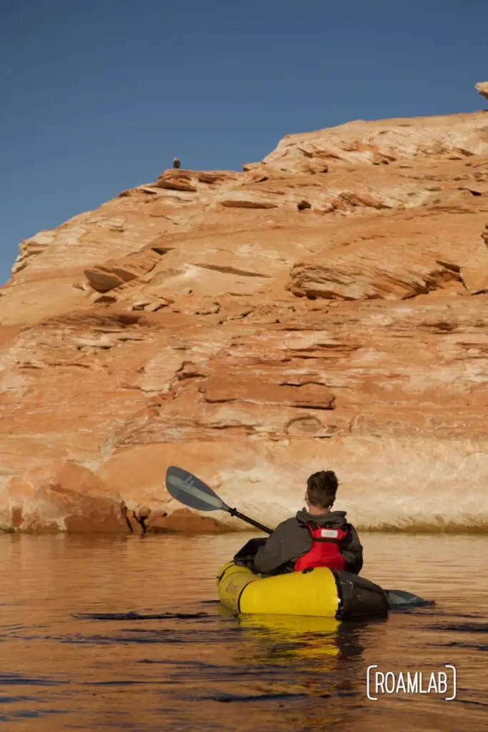 Man paddling in a yellow raft looking up at a bald eagle on the red cliffs on the south shore of Lake Powell.