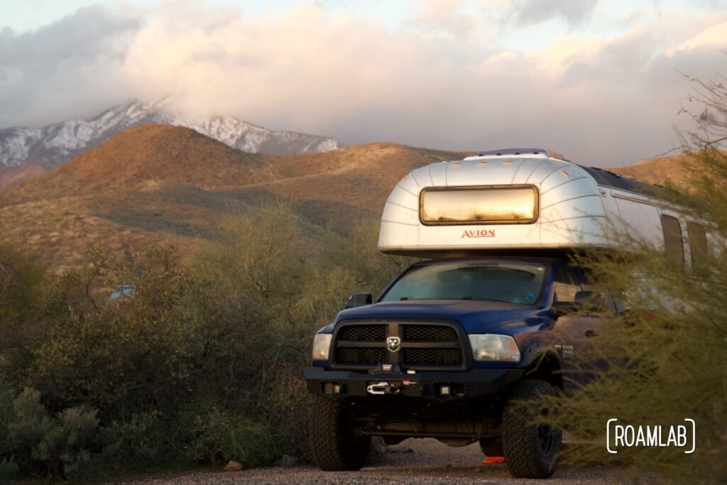 Avion C11 truck camper parked among desert scrub brush with a mountain peak wrapped in clouds in the background.