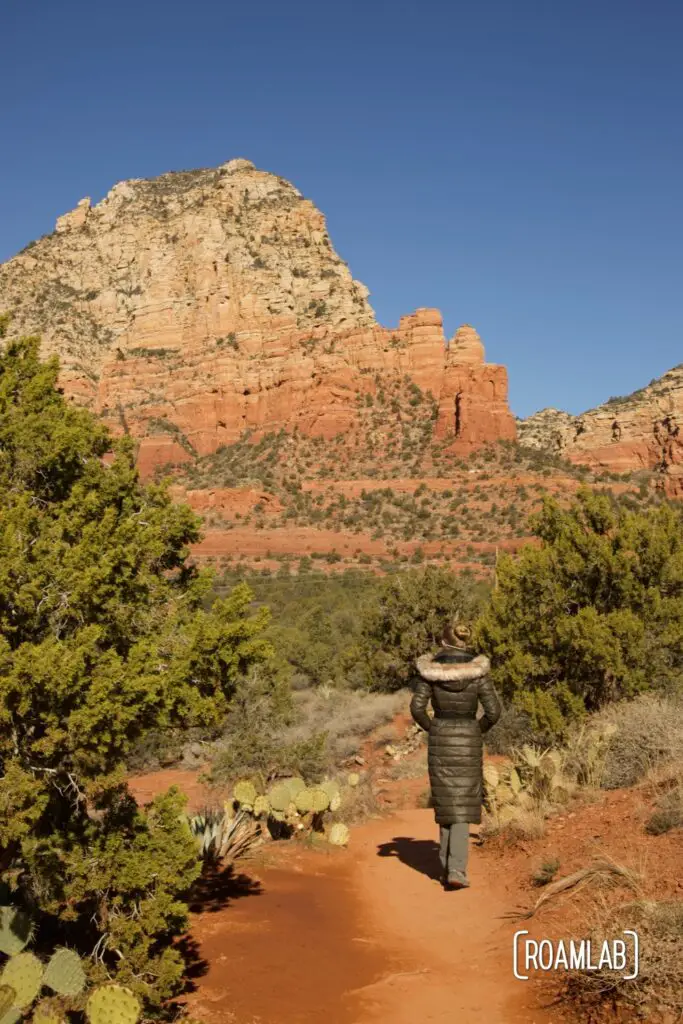 Woman walking down Sugarloaf Loop Trail towards red rock bluffs in Sedona, Arizona.