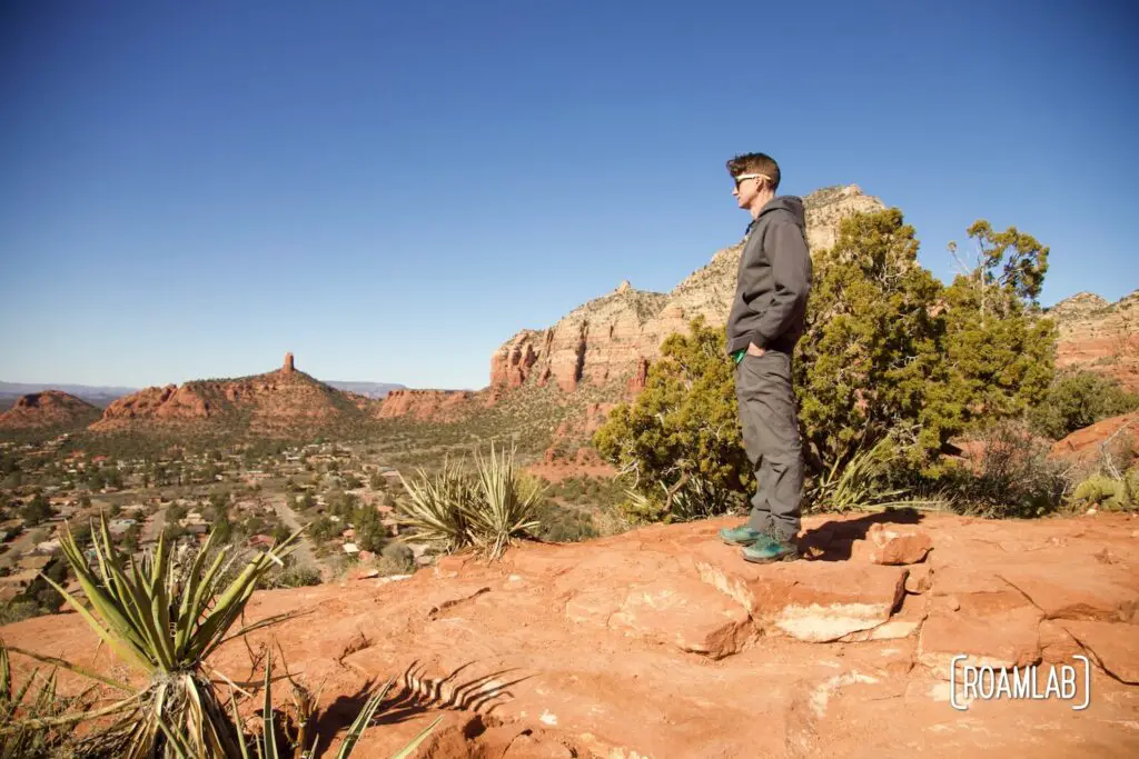 Man standing on a red rock plateau with the outskirts of Sedona, Arizona in the background.