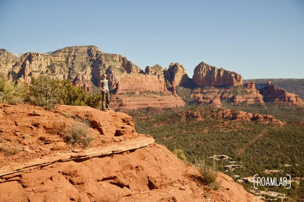 Woman standing on Sugarloaf Summit, a red rock bluff with colorful Sedona mountains in the background.