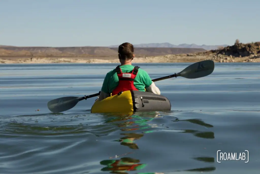 Rear view of Chris paddling in a yellow Kokopelli packraft on the smooth water of Elephant Butte Lake State Park.