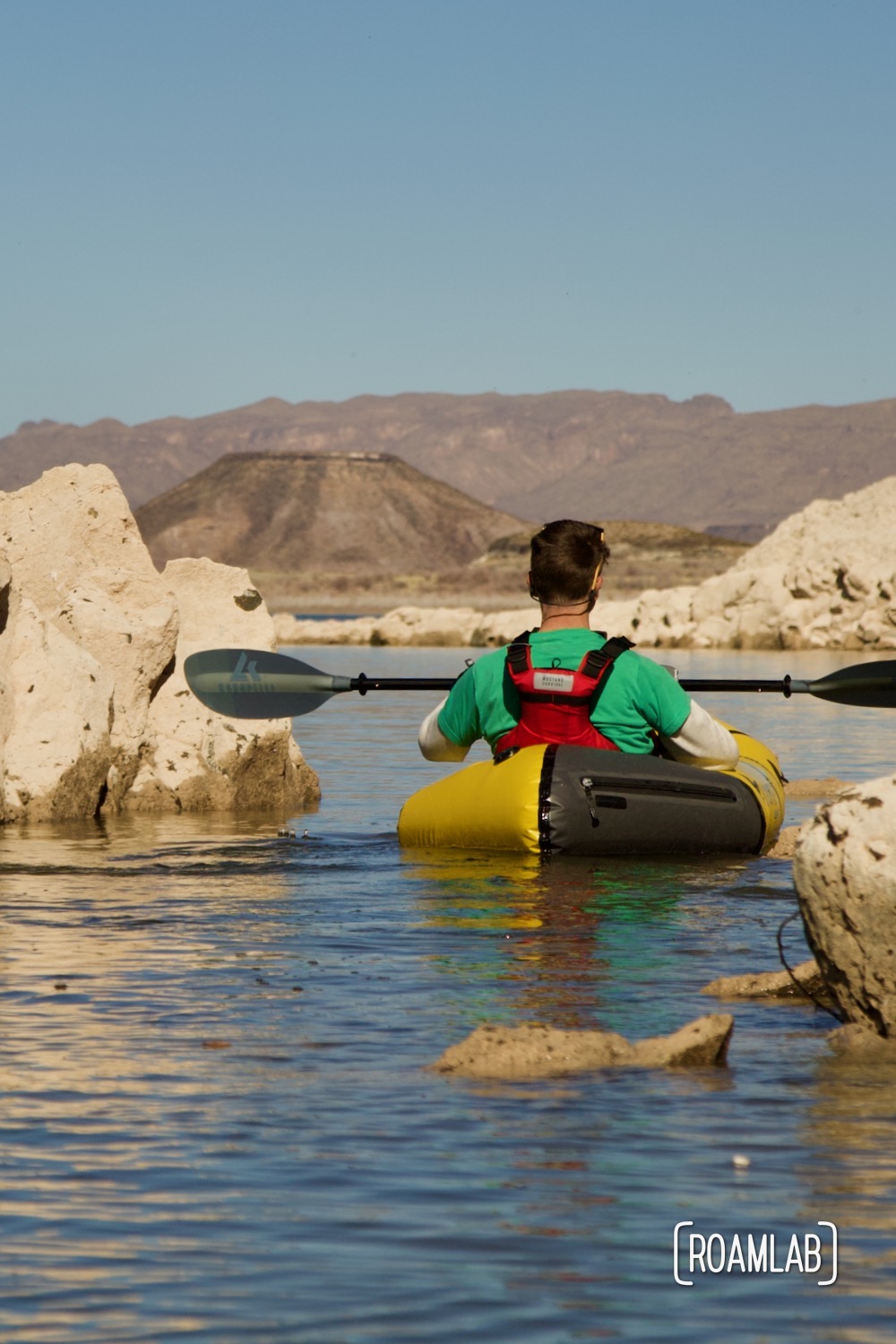 Chris paddling between golden rocks rising out of Elephant Butte Lake in a yellow Kokopelli packraft.