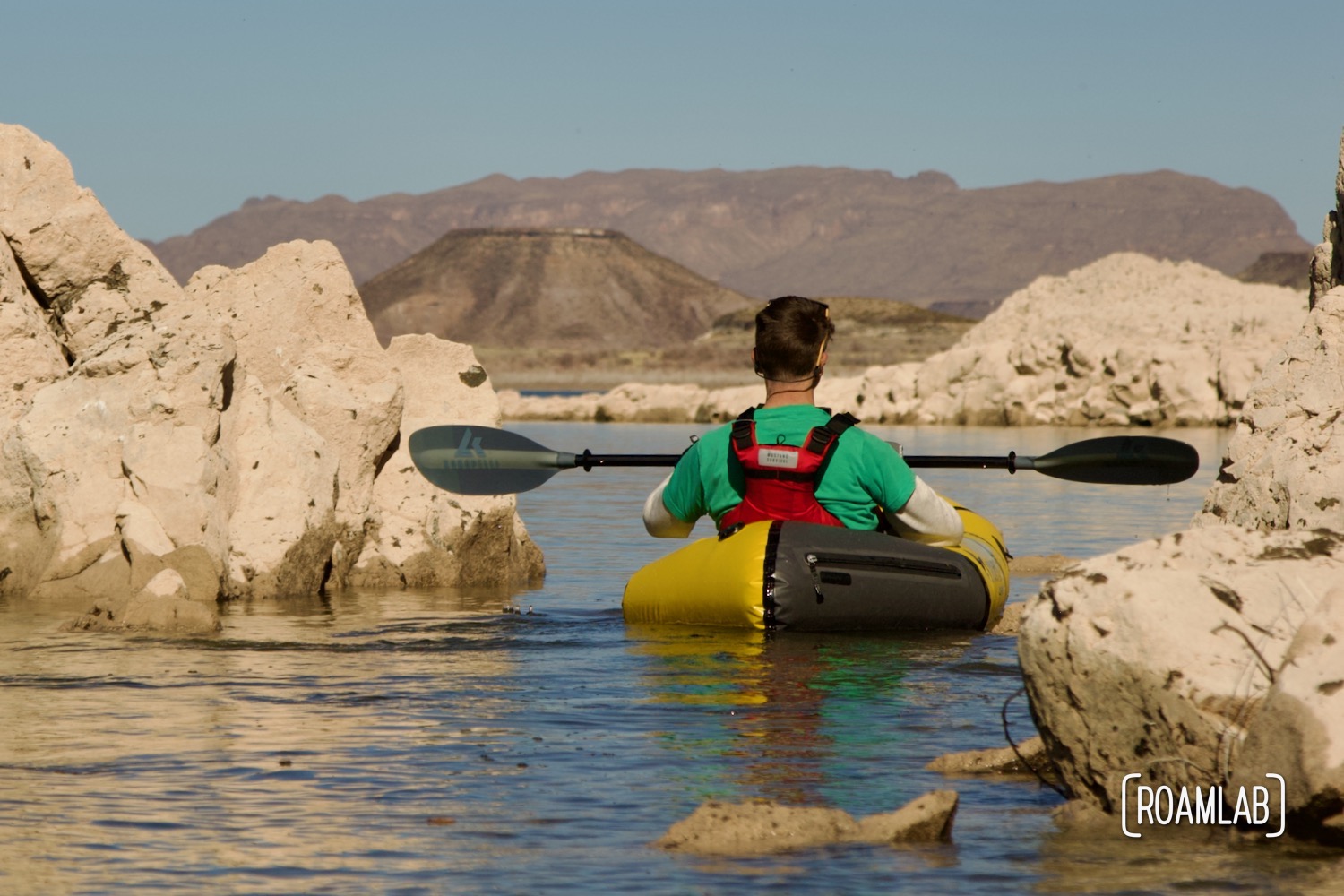 Chris paddling between golden rocks rising out of Elephant Butte Lake in a yellow Kokopelli packraft.