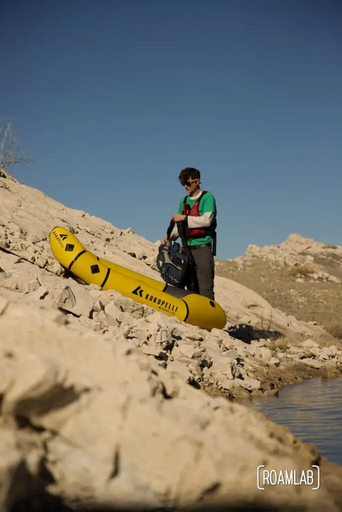Chris stowing a backpack in his Kokopelli packraft along the rocky shoreline of Elephant Butte Lake State Park.