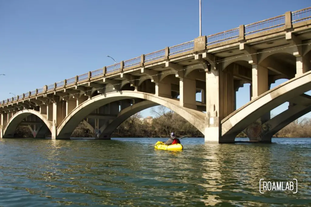 Man paddling in a yellow raft below Lamar Boulevard Bridge in Austin, Texas.