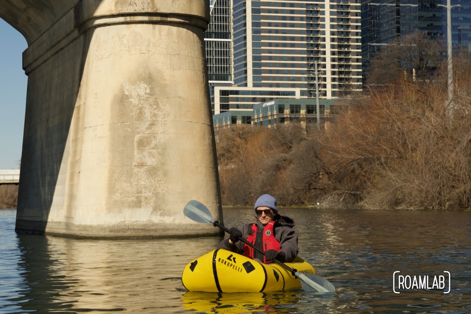 Man paddling by the pillar of Congress Avenue Bridge with Austin, Texas in the background.