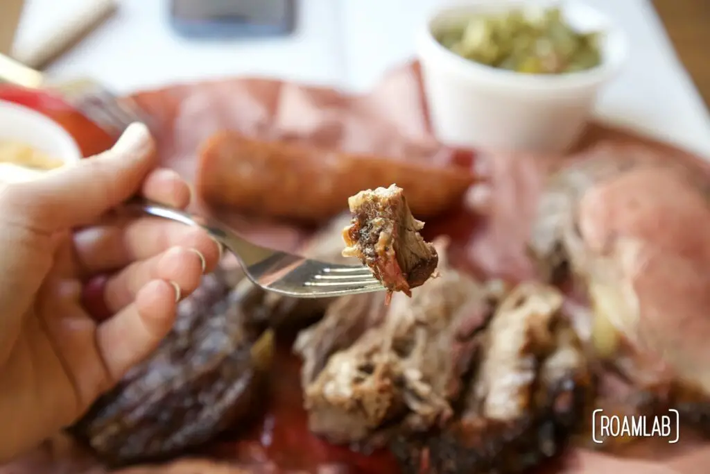 Hand holding a fork with a piece of brisket.