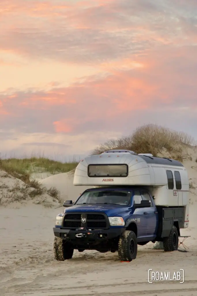 Colorful clouds behind a vintage 1970 Avion C11 truck camper parked on the beach of Padre Island National Seashore in Texas.