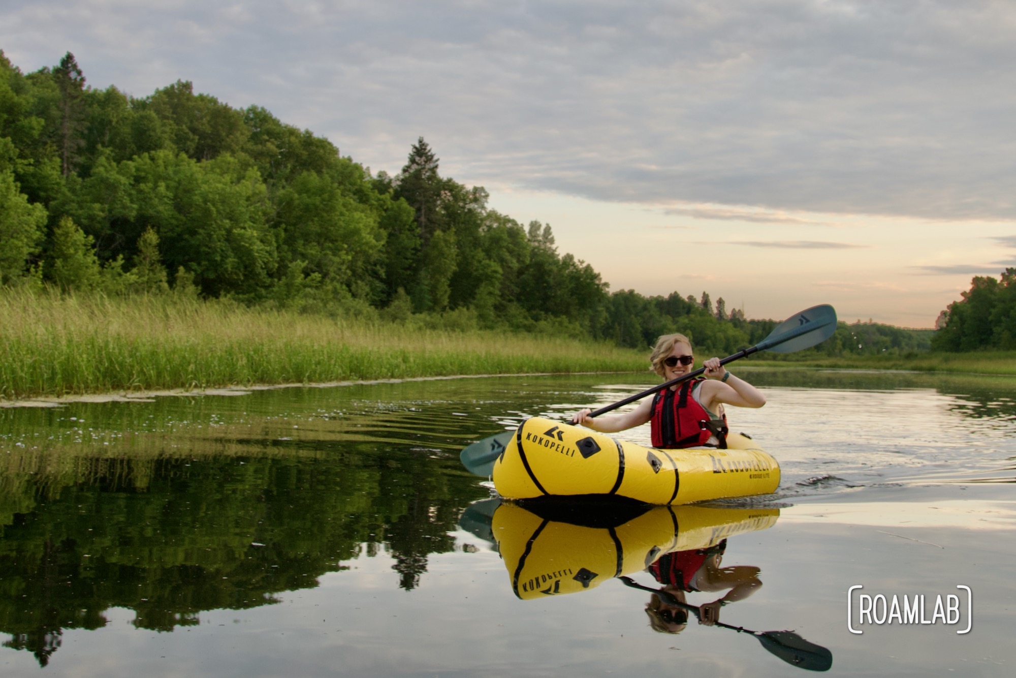 Woman paddling in a yellow raft at sunset.