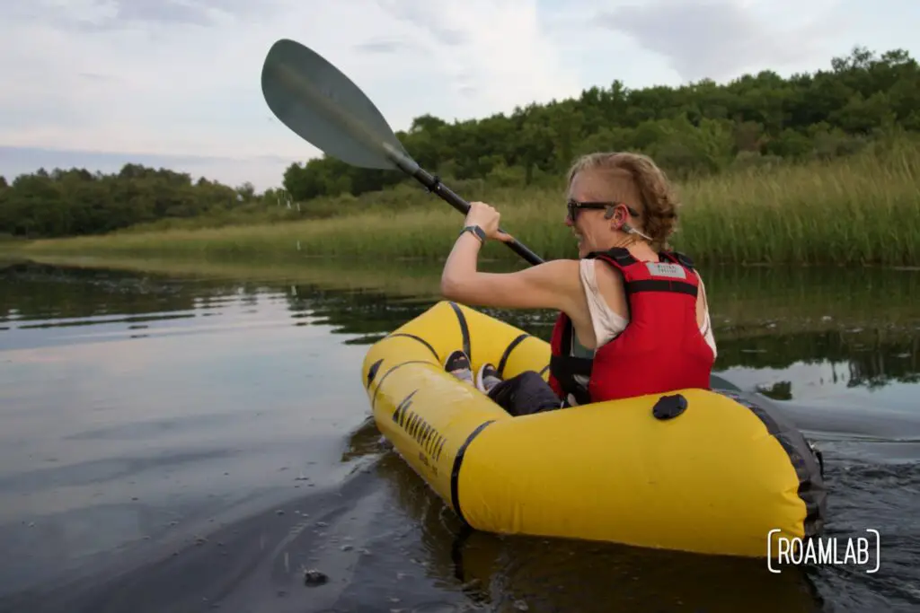 Woman paddling in a yellow raft along a calm river.