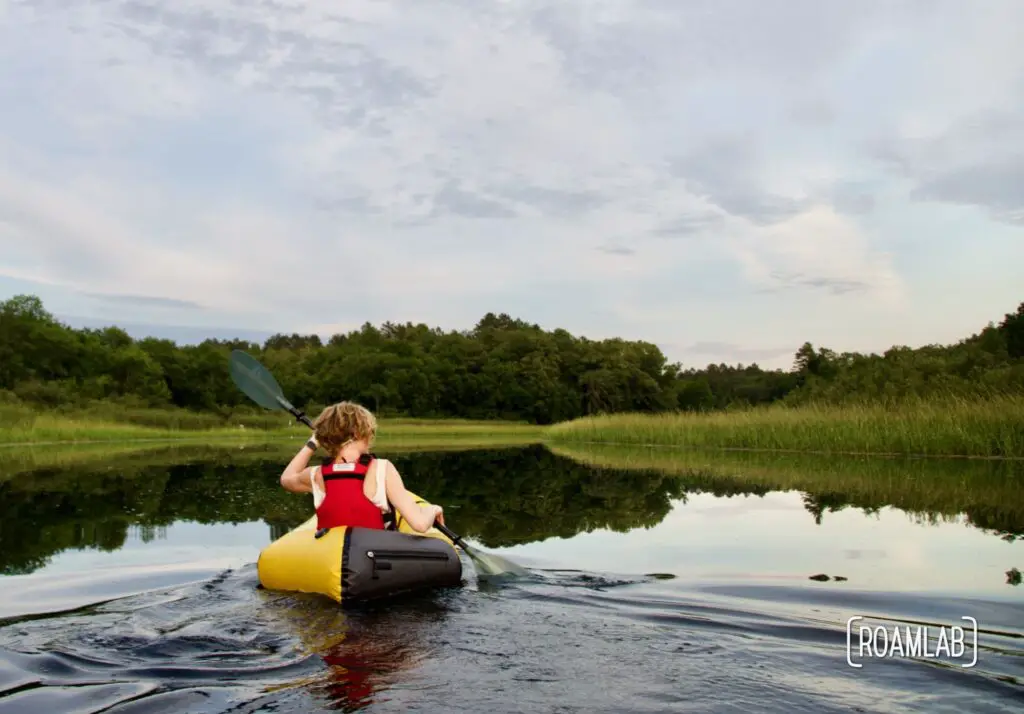 Woman in a yellow raft paddling along a calm river.