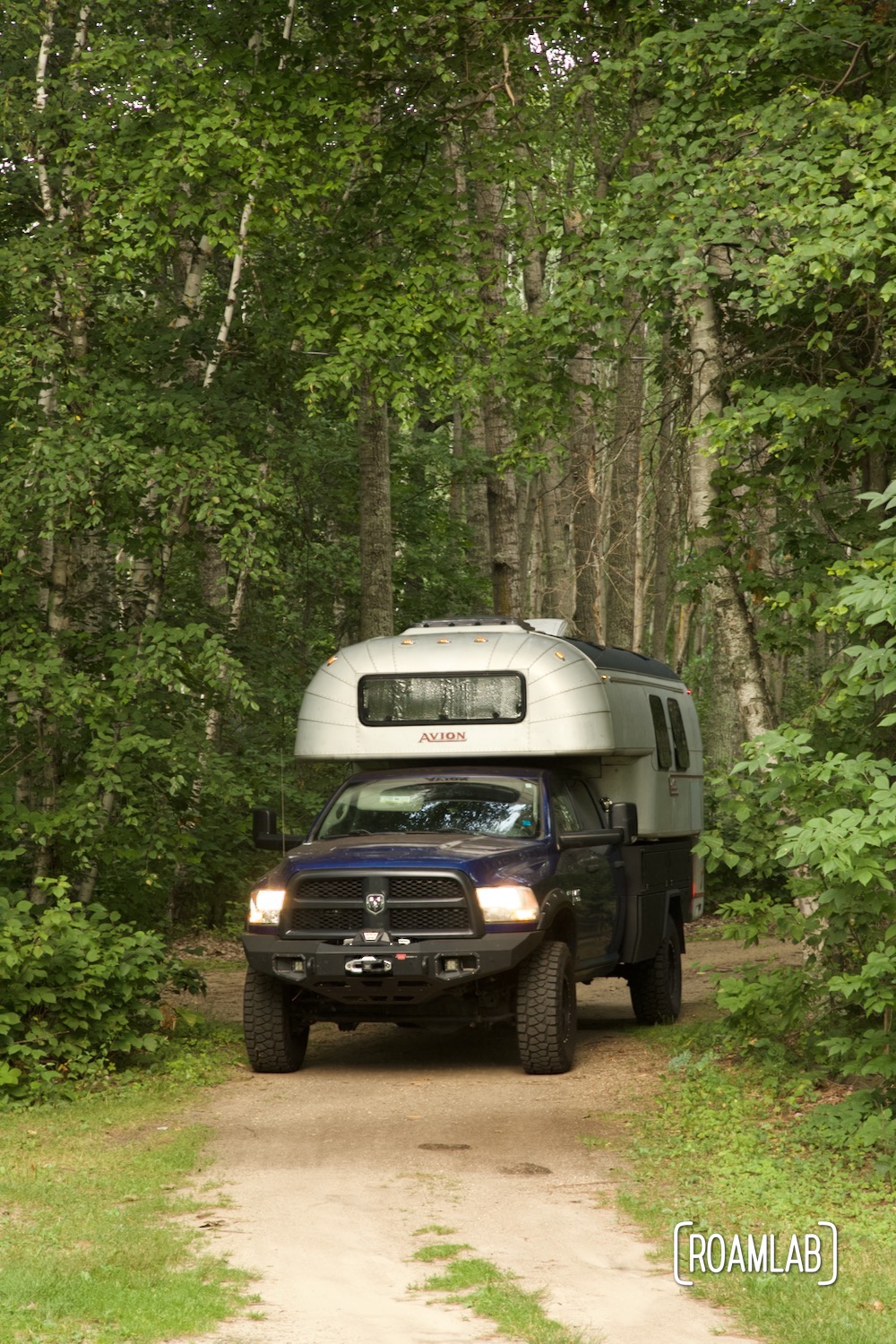 Avion C11 truck camper driving down a dirt road in an aspen forest.