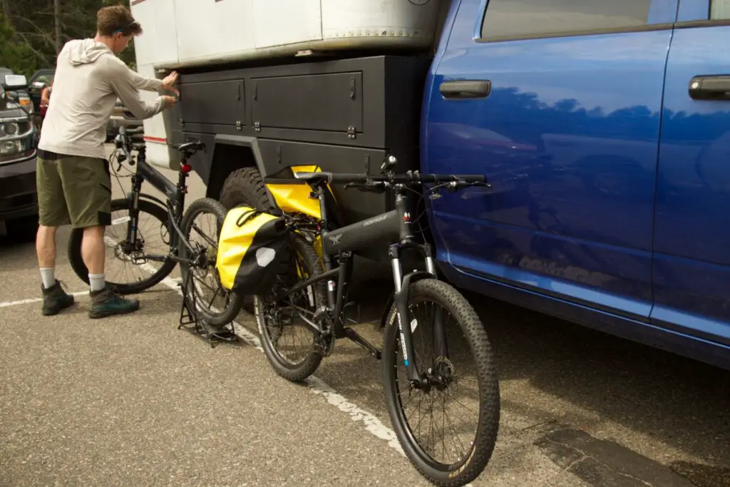 Man closing a storage bin next to two black mountain bikes.