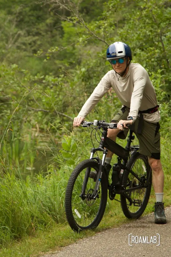 Man on a bike next to a reed lined river.