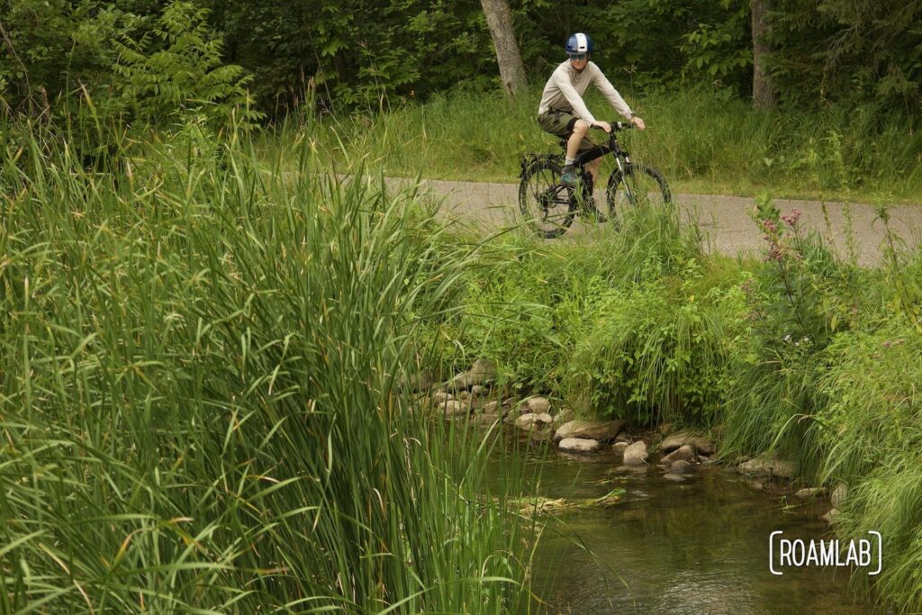Man on a bike pausing along a small river.