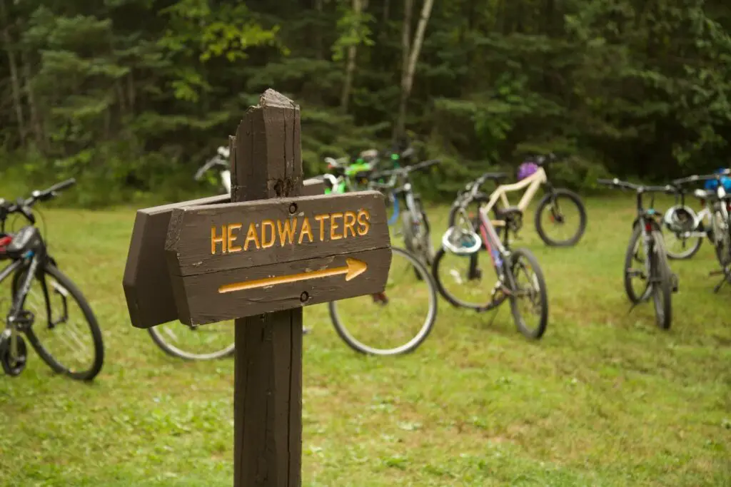 Wooden sign with "Headwaters" in yellow with an arrow and bicycles parked behind it.