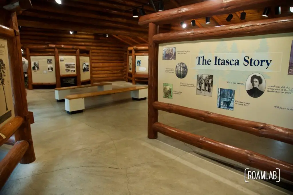 Interior view of a museum with a log cabin asthetic including panels with pictures and explanations of the history and notable aspects of Itasca State Park.