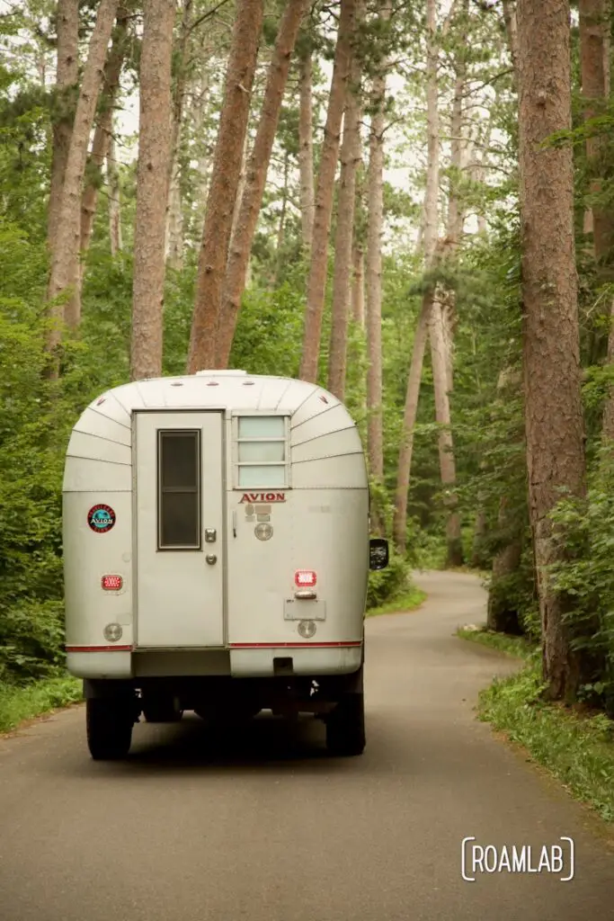 1970 Avion C11 truck camper driving down the winding paved road of Wilderness Drive in Itasca State Park.