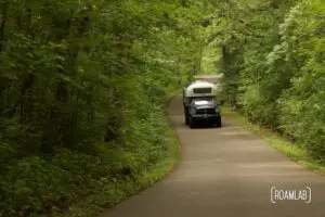 1970 Avion C11 truck camper driving down the winding paved road of Wilderness Drive in Itasca State Park.