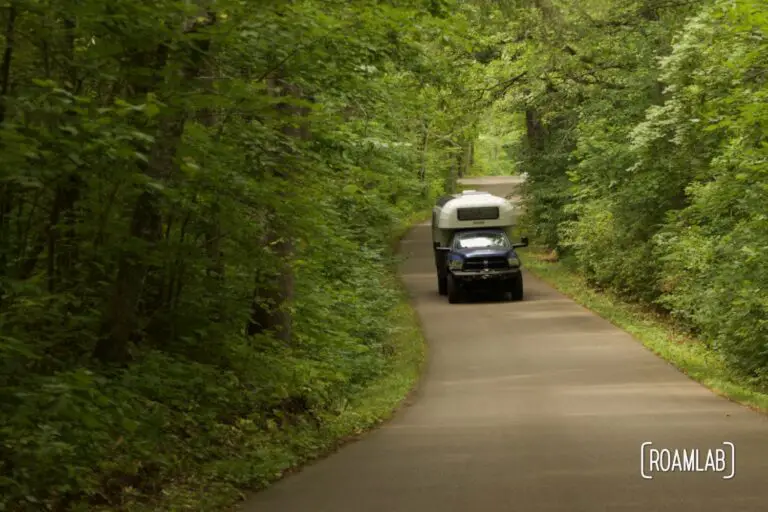 1970 Avion C11 truck camper driving down the winding paved road of Wilderness Drive in Itasca State Park.