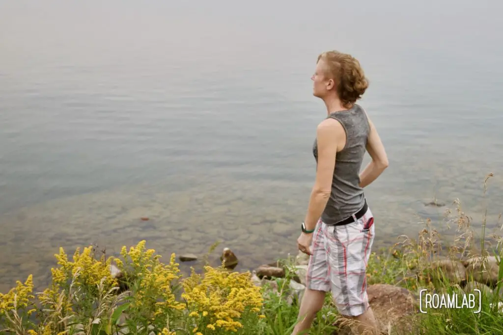 Woman walking by wildflowers next to a grey lake.