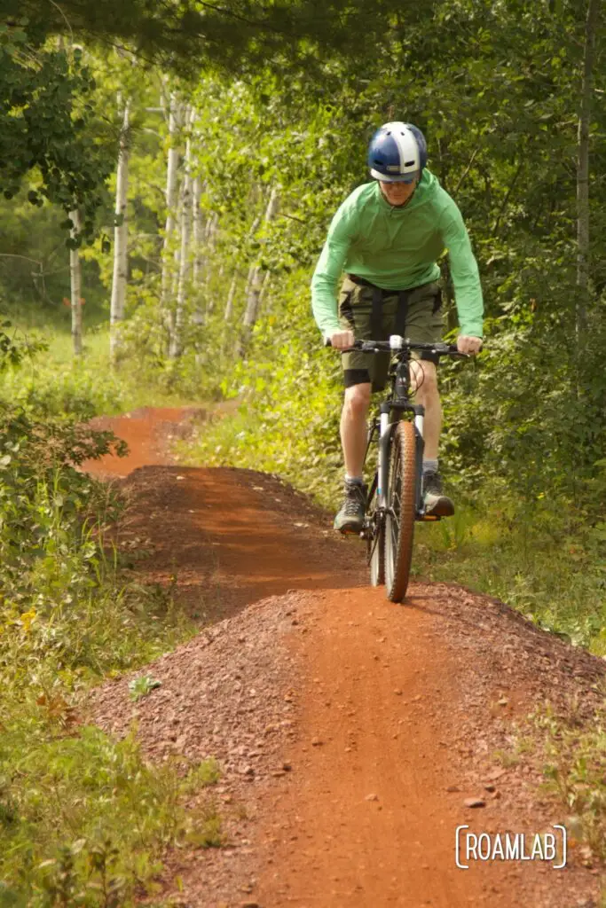 Man on a mountain bike peddling on red dirt single track in a forest.