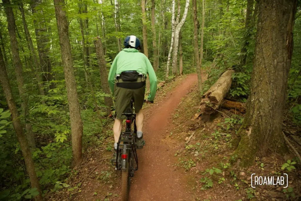 Man on a mountain bike peddling on red dirt single track in a forest.