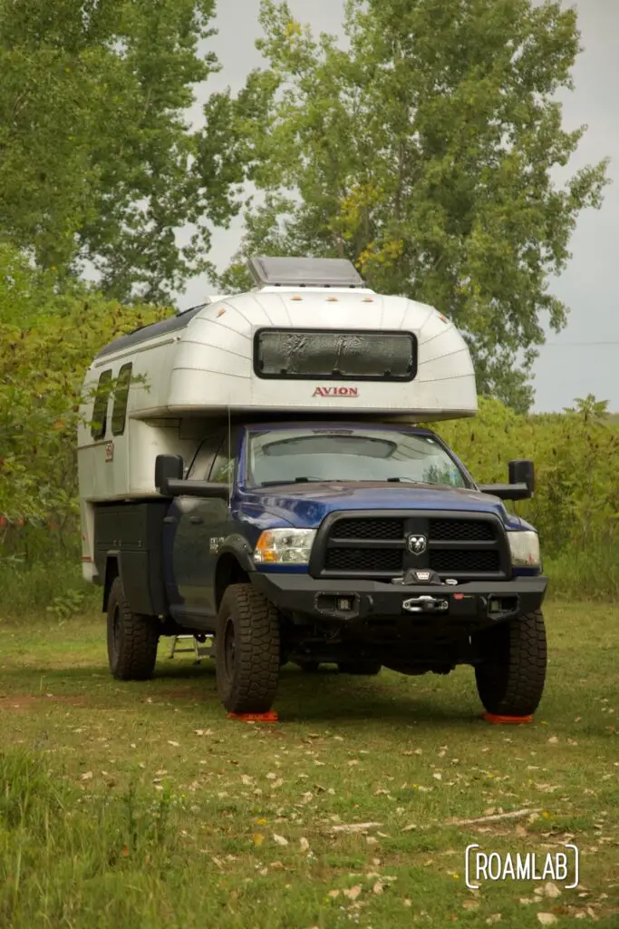 1970 Avion C11 truck camper parked in a green field surrounded by wild sumac