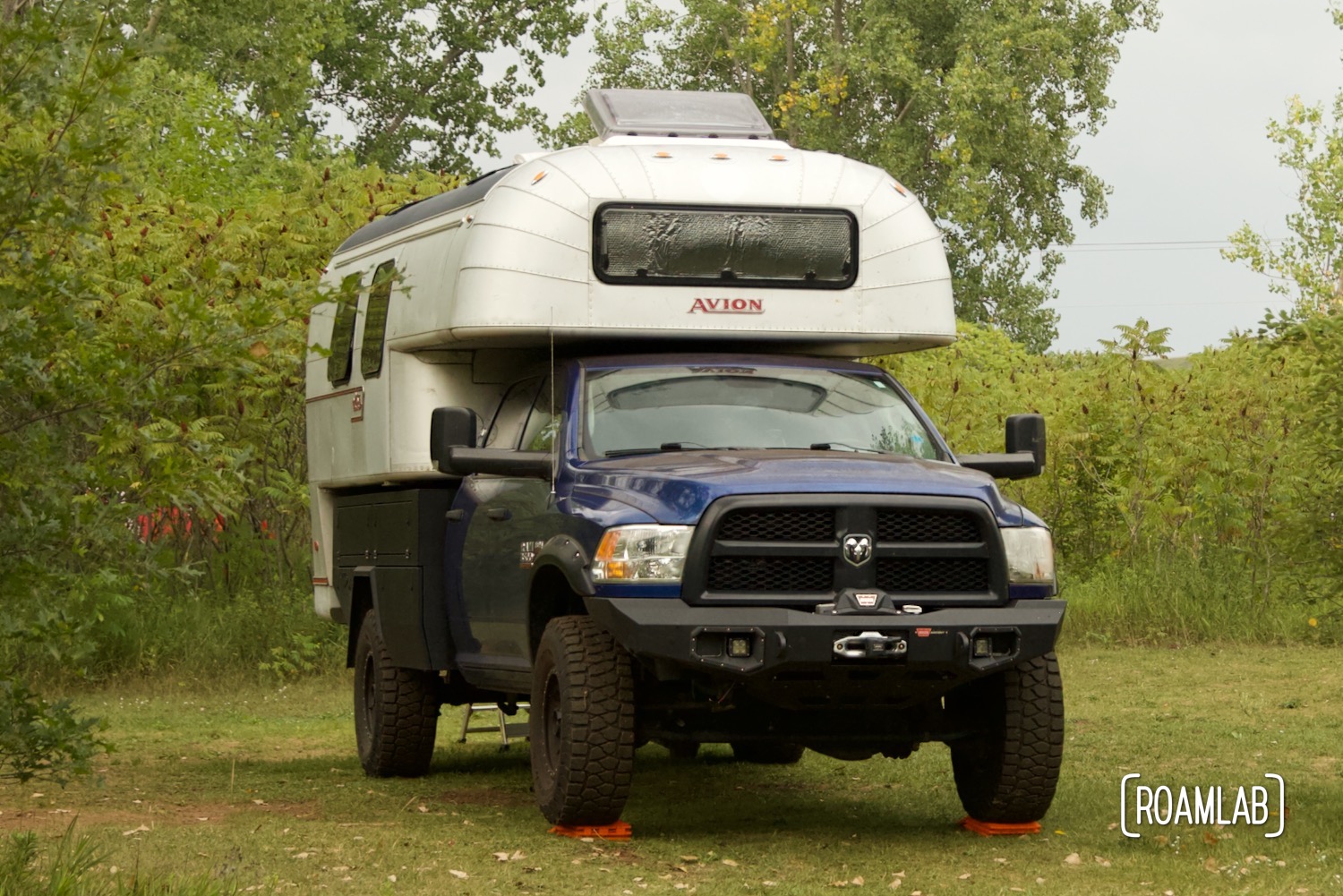 1970 Avion C11 truck camper parked in a green field surrounded by wild sumac