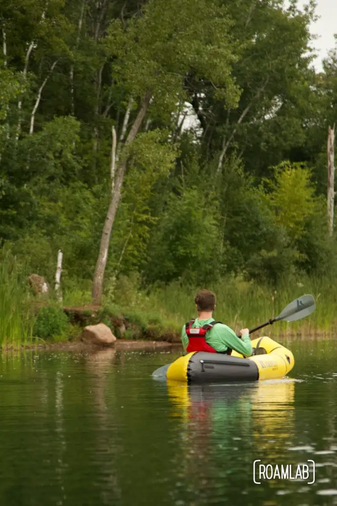 Man paddling a yellow raft along a forested shoreline in Cuyuna Country State Recreation Area.