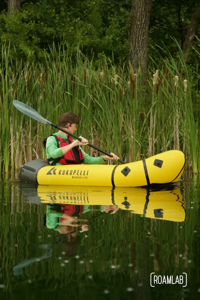 Man paddling a yellow raft along a reedy shoreline in Cuyuna Country State Recreation Area.