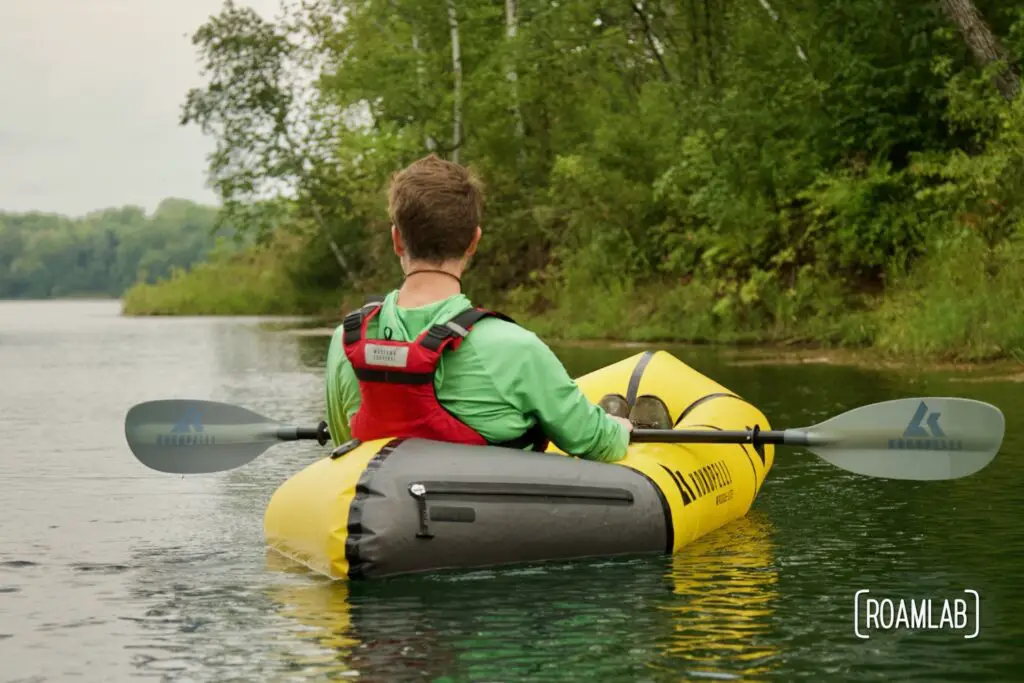 Man in a yellow raft staring off into the distance along a forested shoreline in Cuyuna Country State Recreation Area.