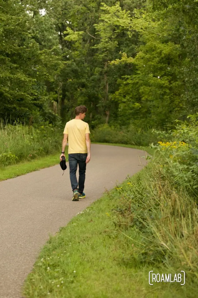 Man walking down a paved trail into a green forest.