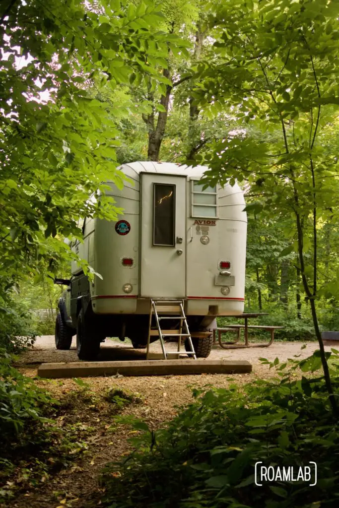 Rear view of a 1970 Avion C11 truck camper parked in a forested campsite.