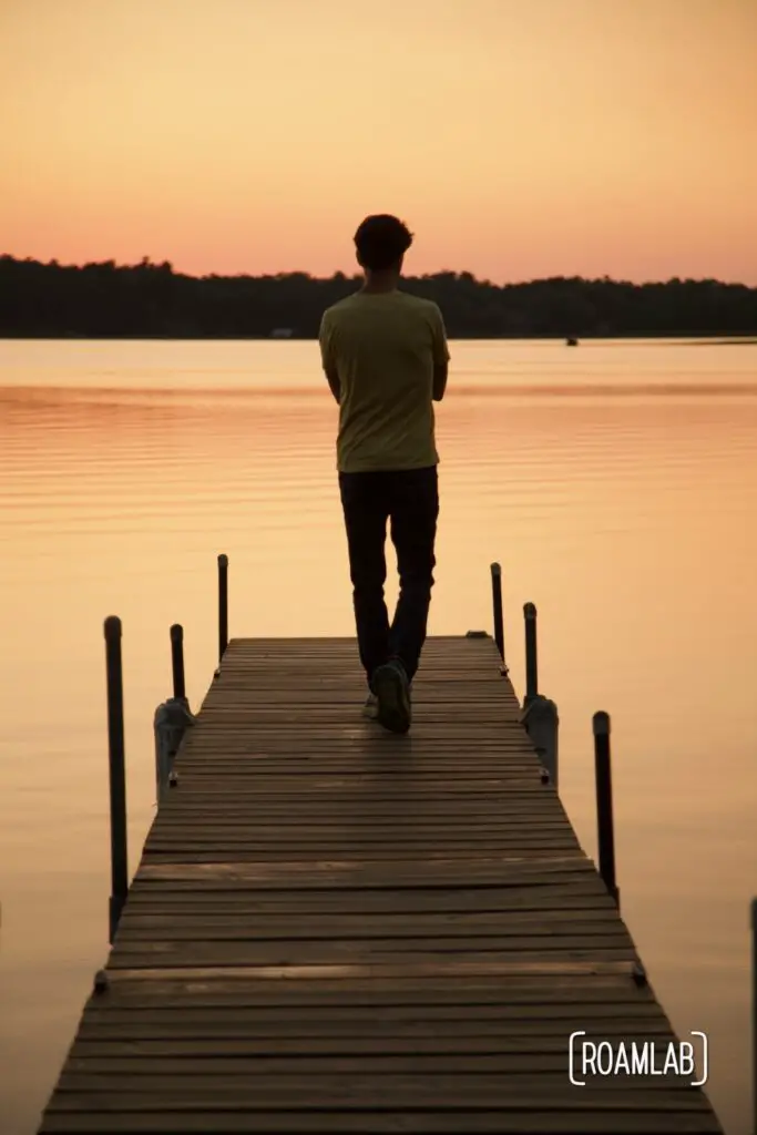 Man walking along a dock at sunset.