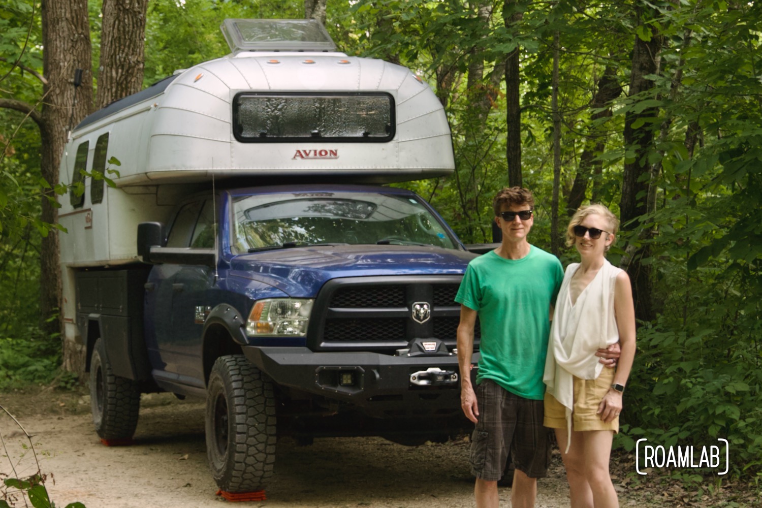 Man and woman standing in front of a vintage truck camper in the forest.