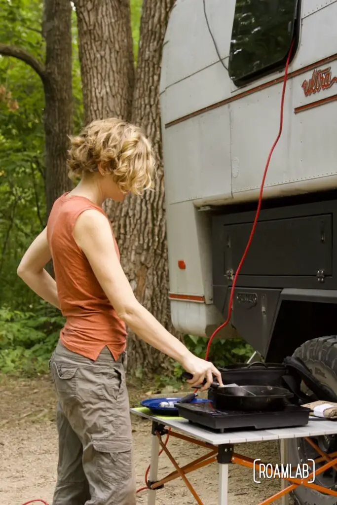 Woman cooking on a stove outside a vintage truck camper.