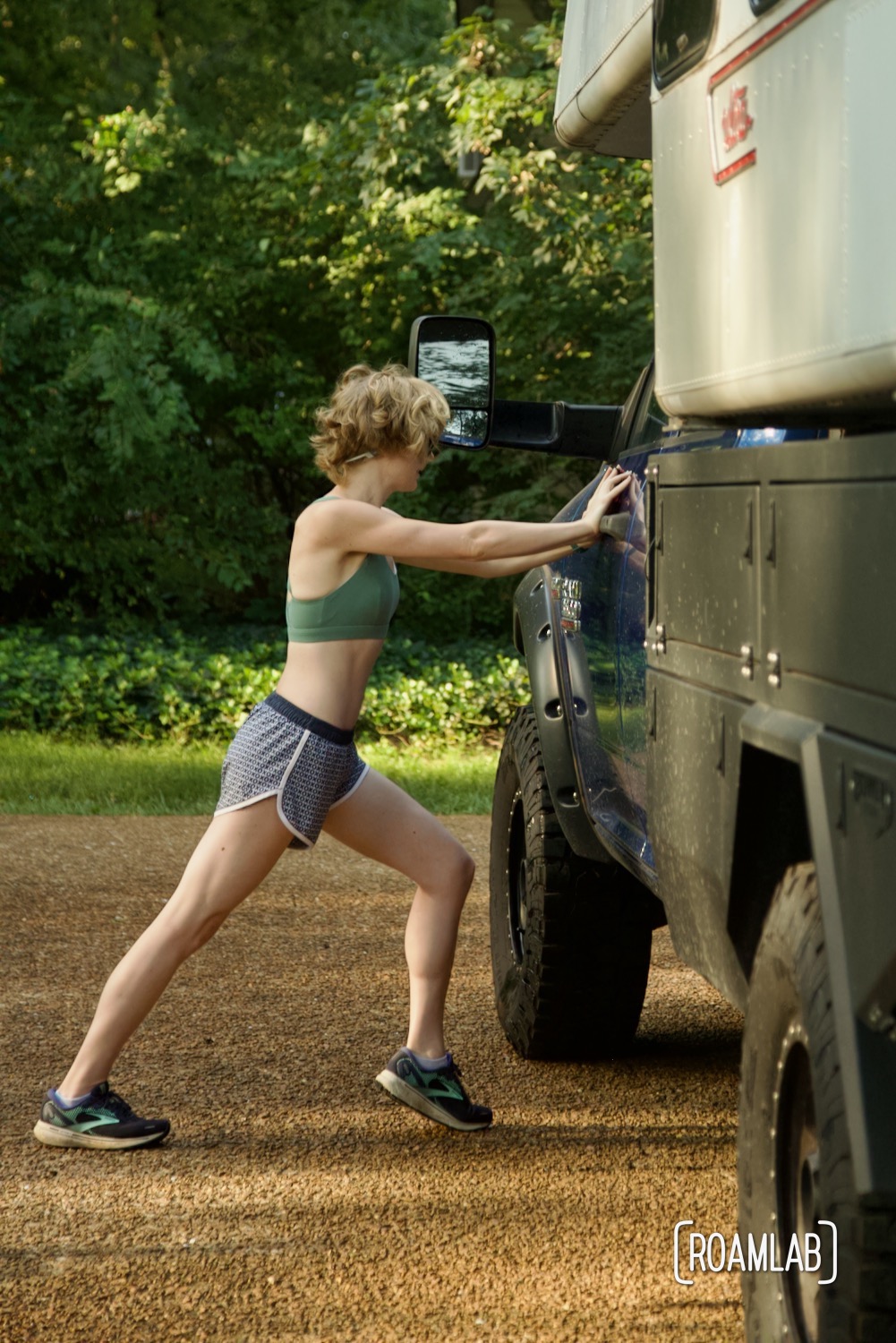 Woman pushing against a truck to stretch her calf muscle.