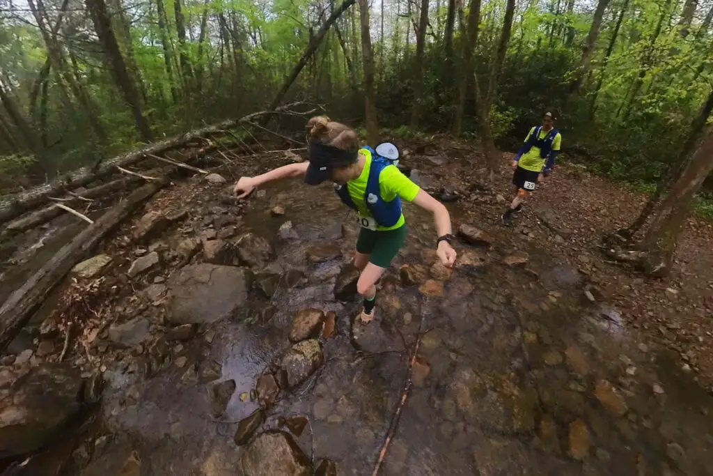 Man and woman trail runners hopping across Rock Creek after Aid Station 1.