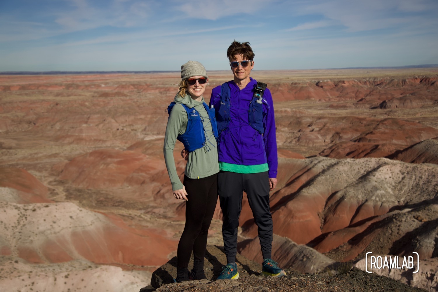 Man and woman in trail running gear standing together over the red buttes of Kachina Point.