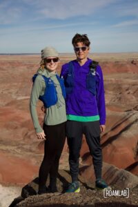 Man and woman in trail running gear standing together over the red buttes of Kachina Point.