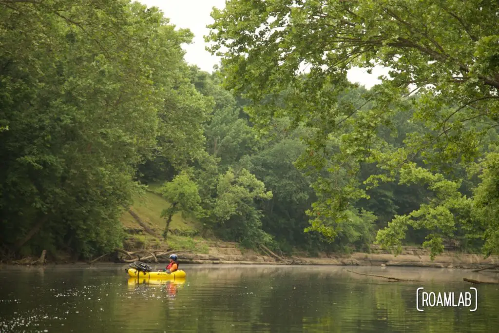 Landscape view of a tree lined river with a bright yellow raft in the distance.