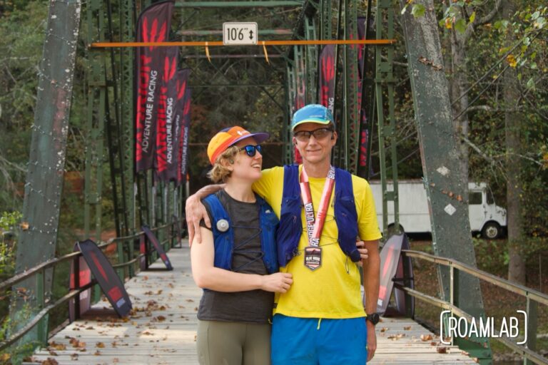 Man and woman in running gear standing at the Blue Ridge Ultra finish line with a bridge in the background.