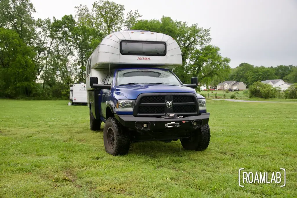 Truck camper parked in a large green field on a cloudy day.