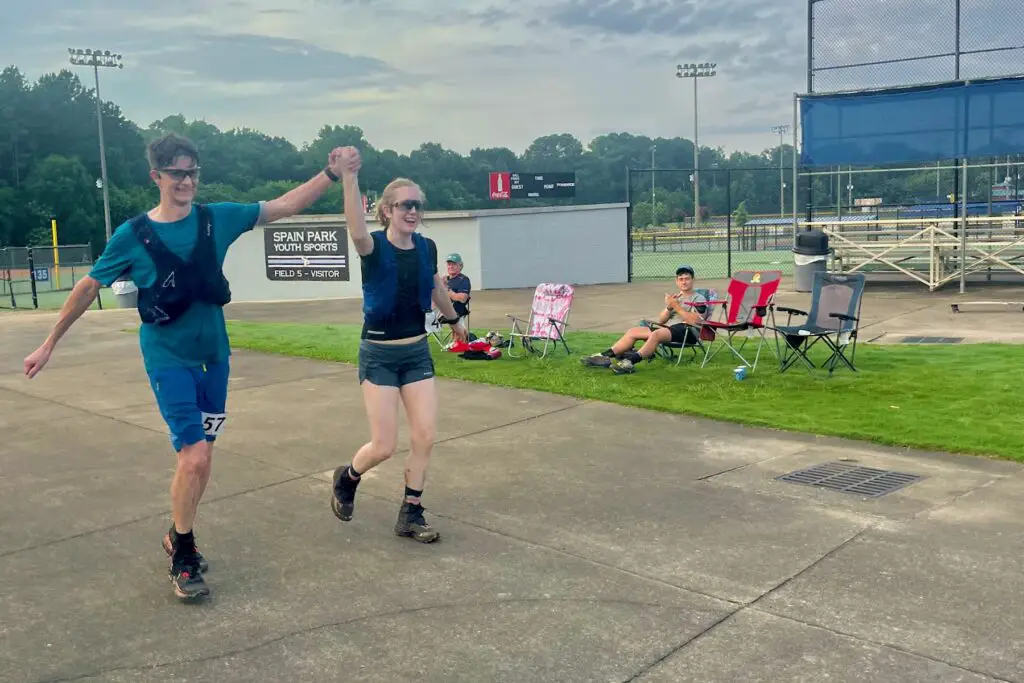 Man and woman, drenched in sweat, triumphantly holding up their hands.