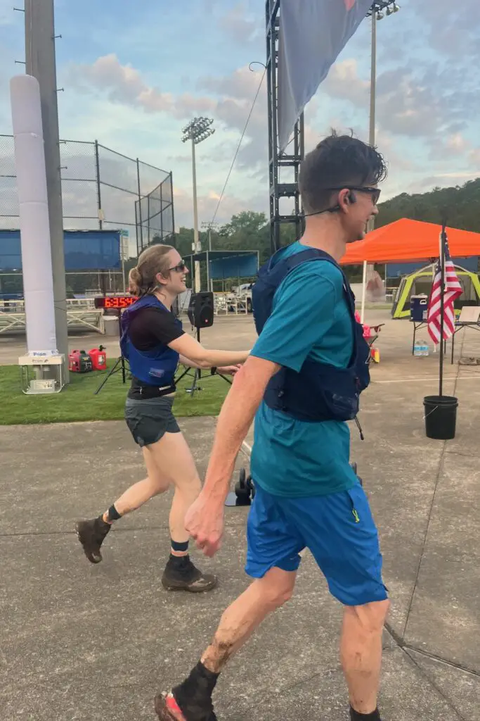 Man and woman, drenched in sweat, holding hands while crossing a finish line.